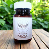 Full Spectrum CBD Capsules in a bottle with a white lid on a wooden table with greenery in the background